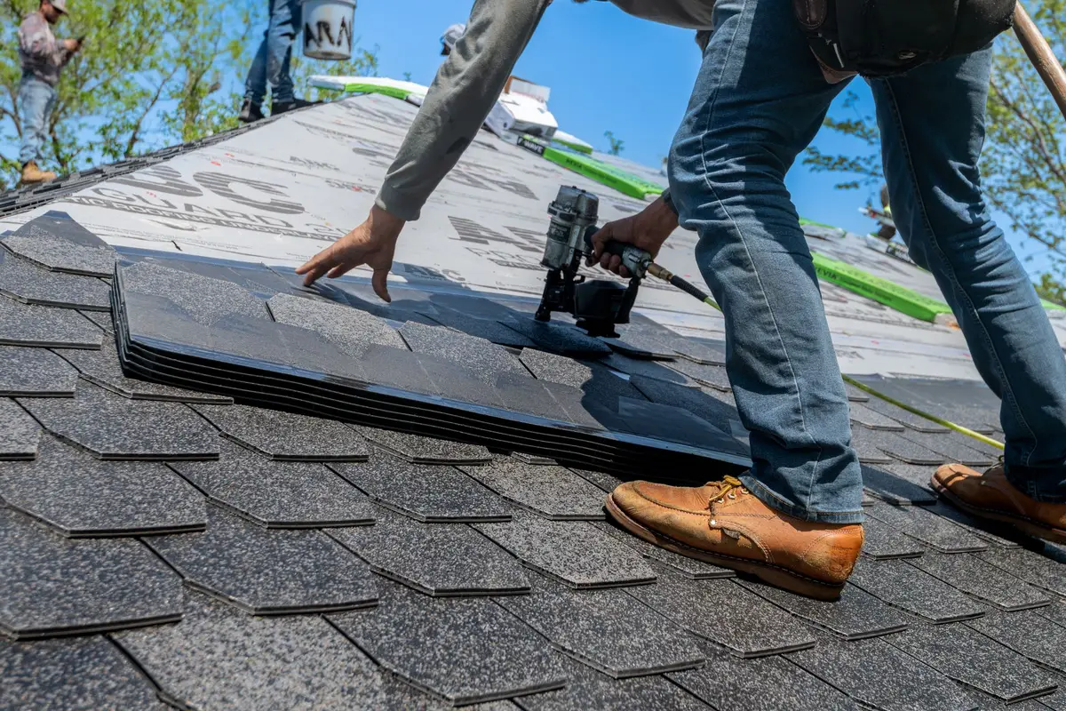 Roofer’s hands and boots on a residential roof while new asphalt shingles are nailed down